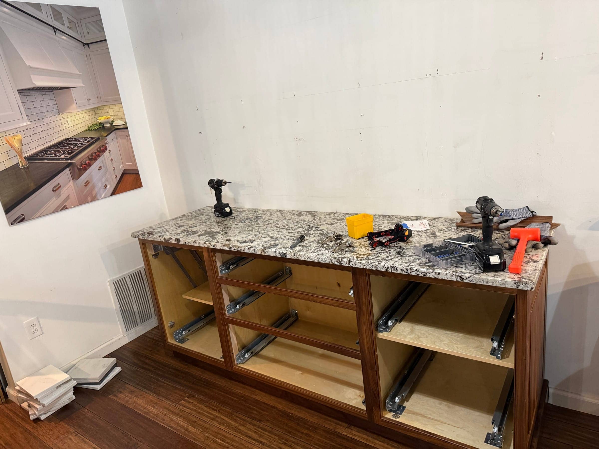 Cabinet base with a granite top being assembled against a wall, drills and tools on the counter