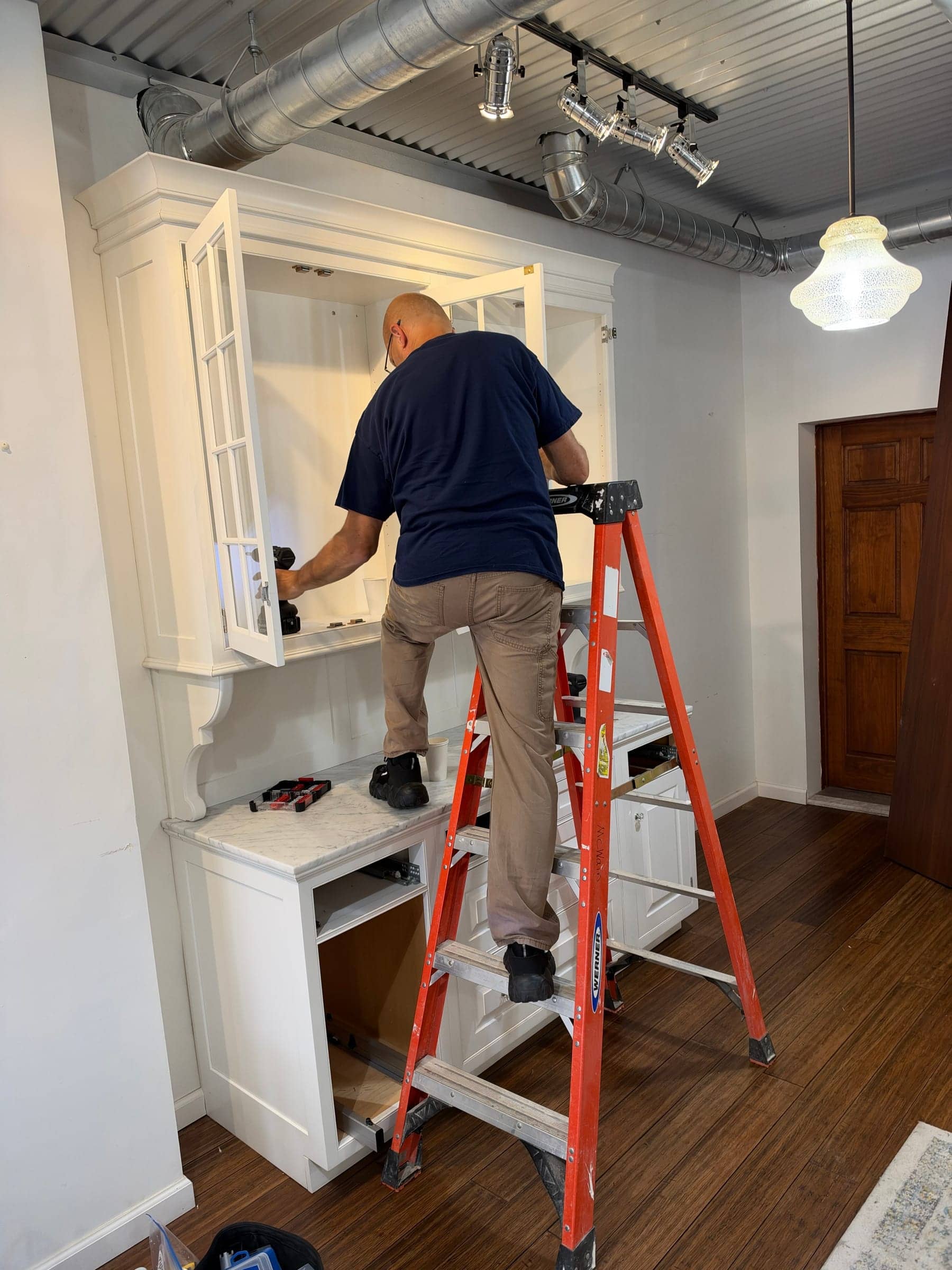McWain crew member on an orange ladder fitting the upper section of a white built-in hutch