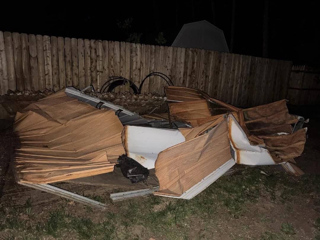 Broken-down panels and debris piled against a wood fence at night, ready to load