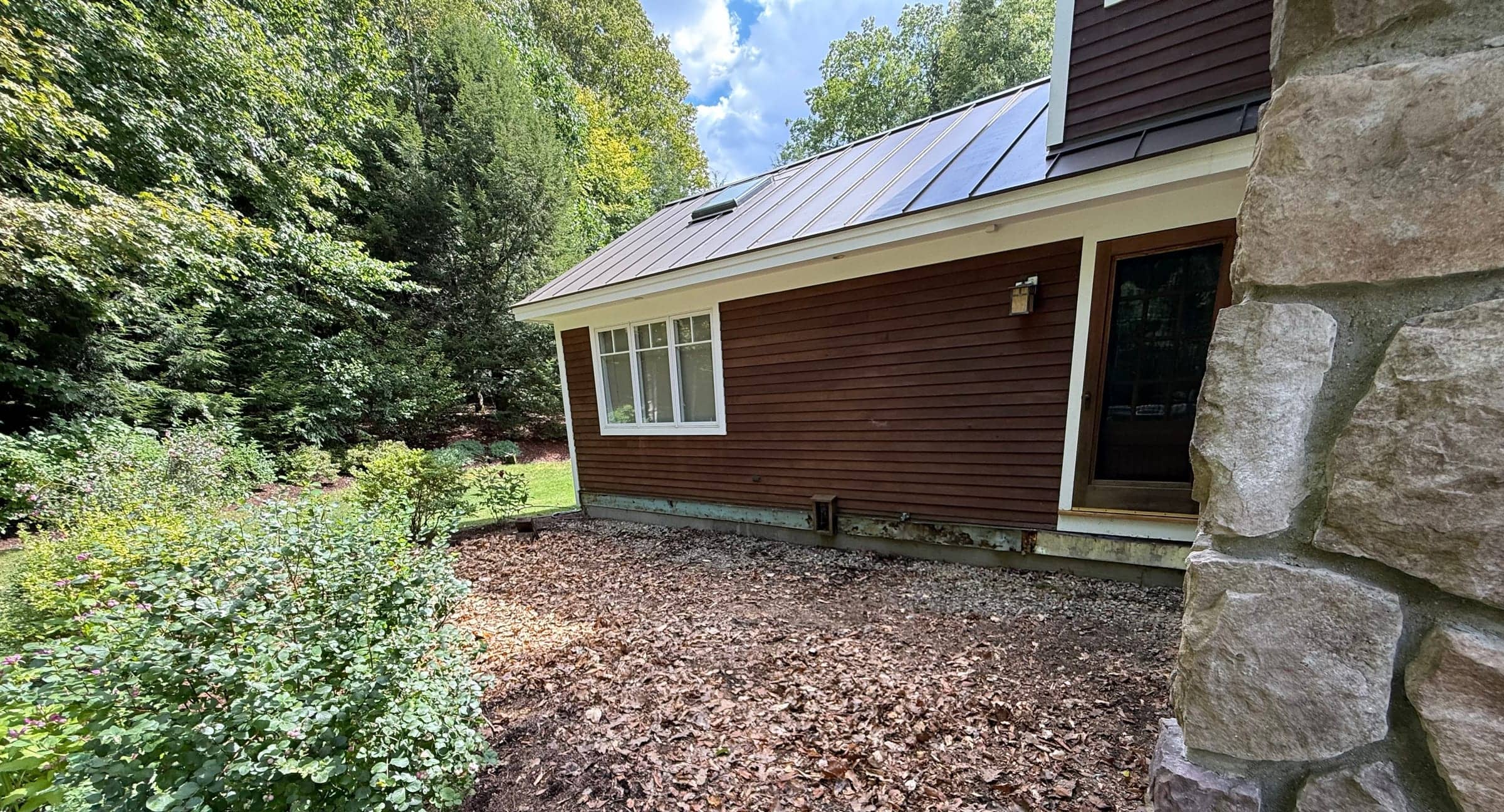 Side of a brown-sided house after a deck was removed: bare mulched ground where the deck stood