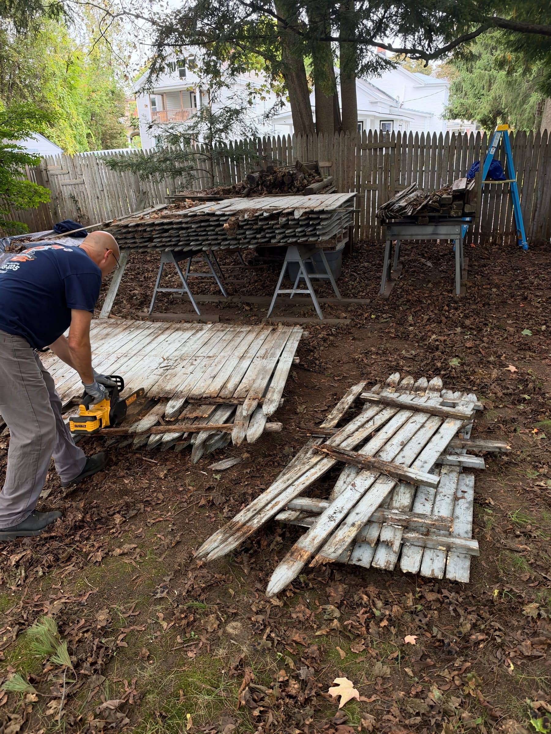 A McWain crew member cutting old fence panels down to size with a power saw in a backyard
