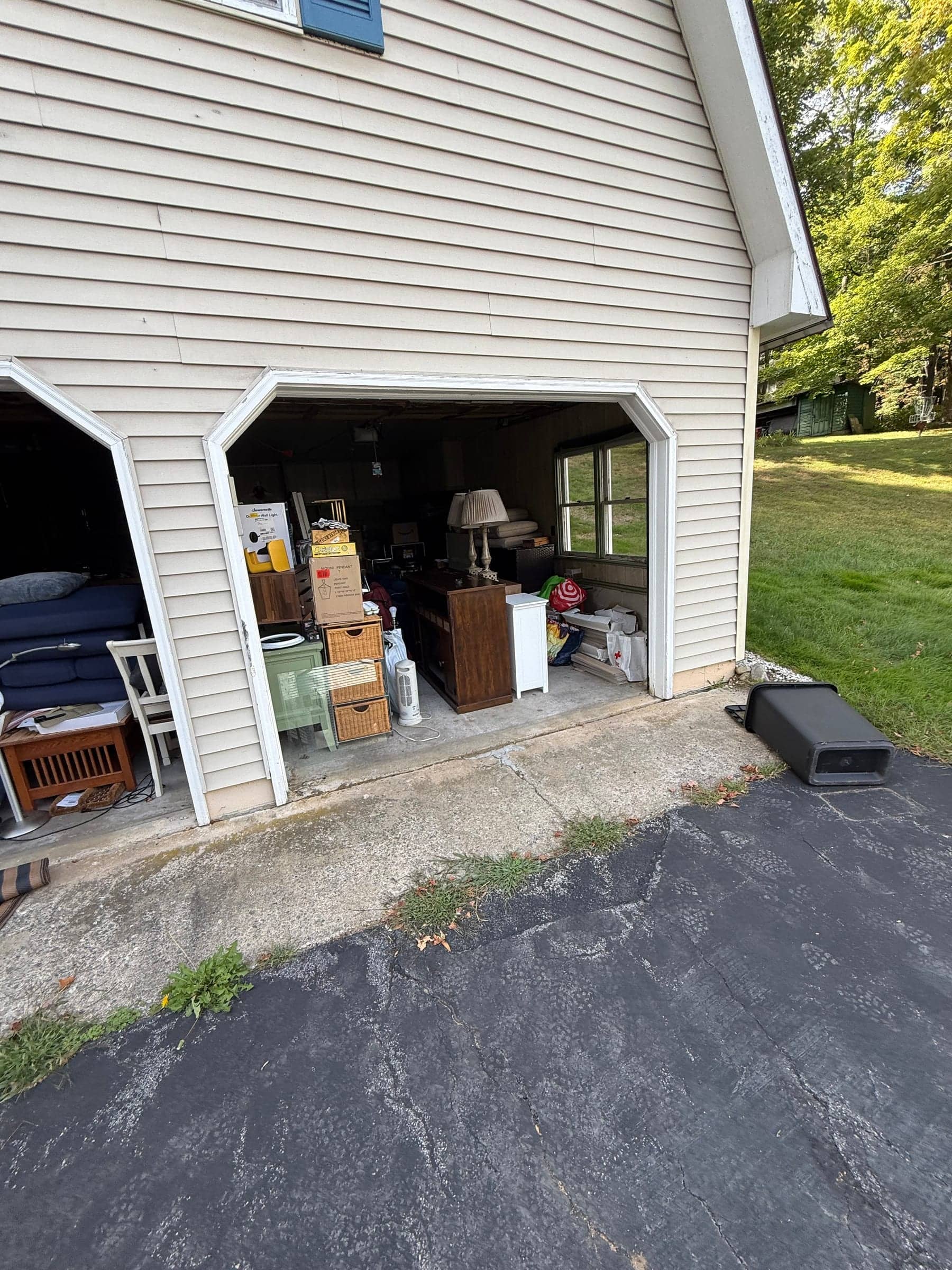 Two-car garage with the doors open, full of furniture, boxes, a lamp and stored household items
