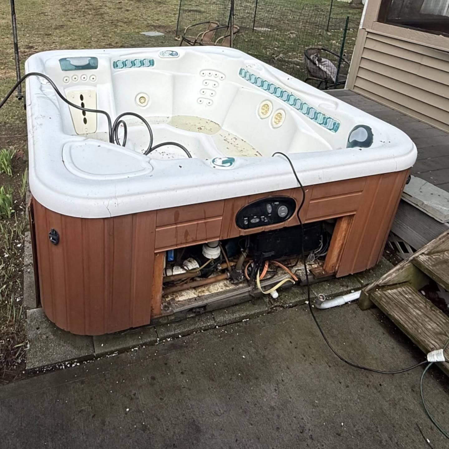 Old hot tub with its side panel off and wiring exposed, before removal