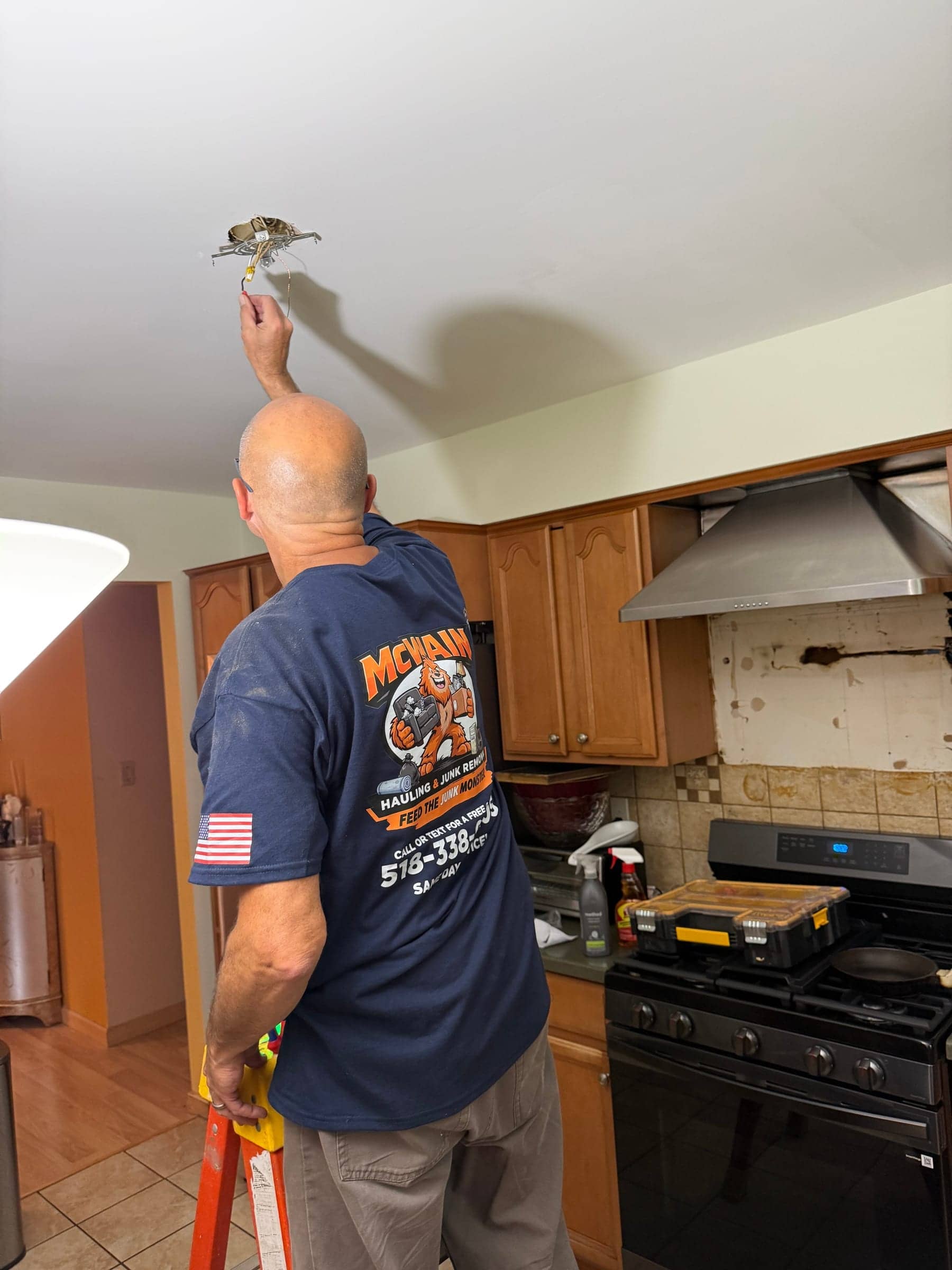 McWain crew member on a ladder wiring a ceiling light fixture in a kitchen