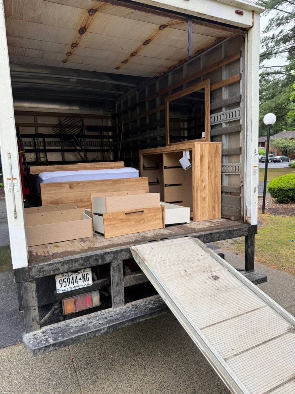 McWain box truck with ramp down, loaded with dresser drawers, a mattress and wood furniture