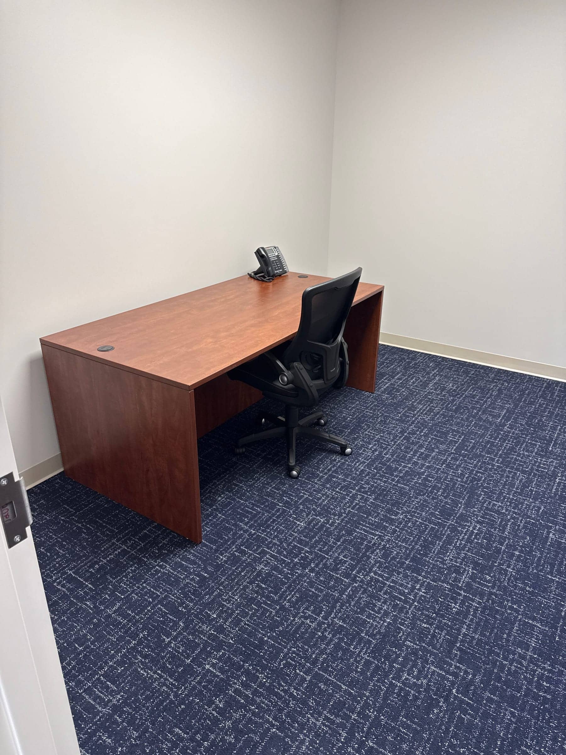 Assembled office desk and black desk chair in an empty office with blue carpet