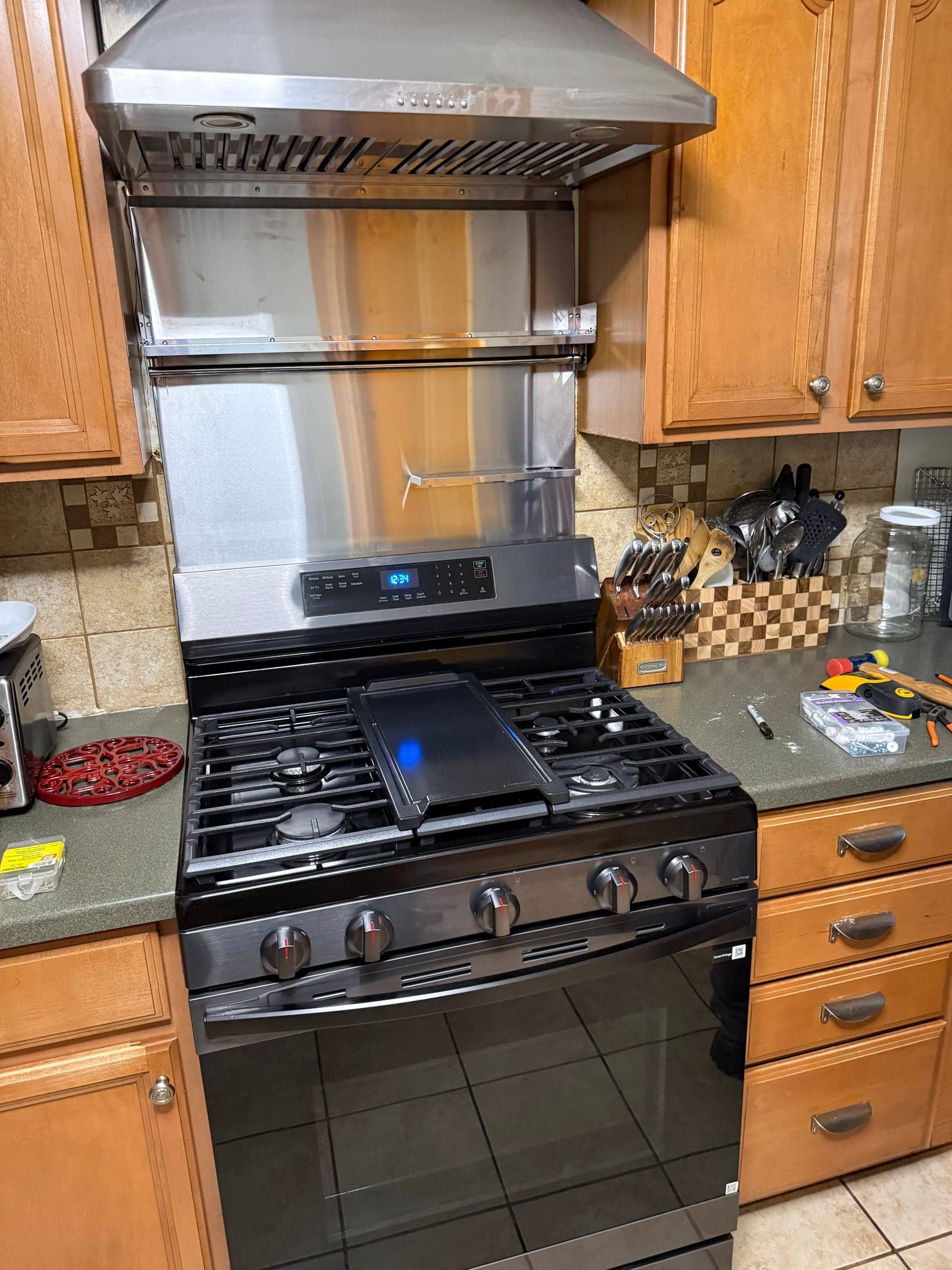 New black gas range installed under a stainless steel hood in a kitchen with wood cabinets