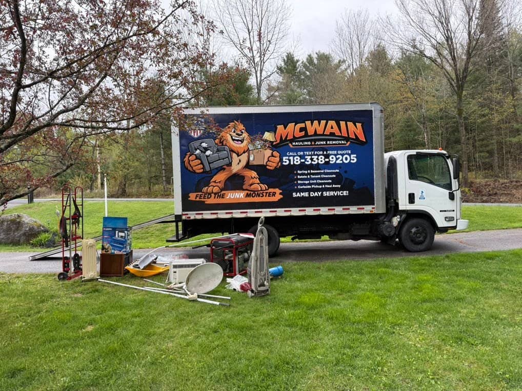 McWain truck in a yard with a cleanout pile staged on the lawn: furniture, a grill and household items