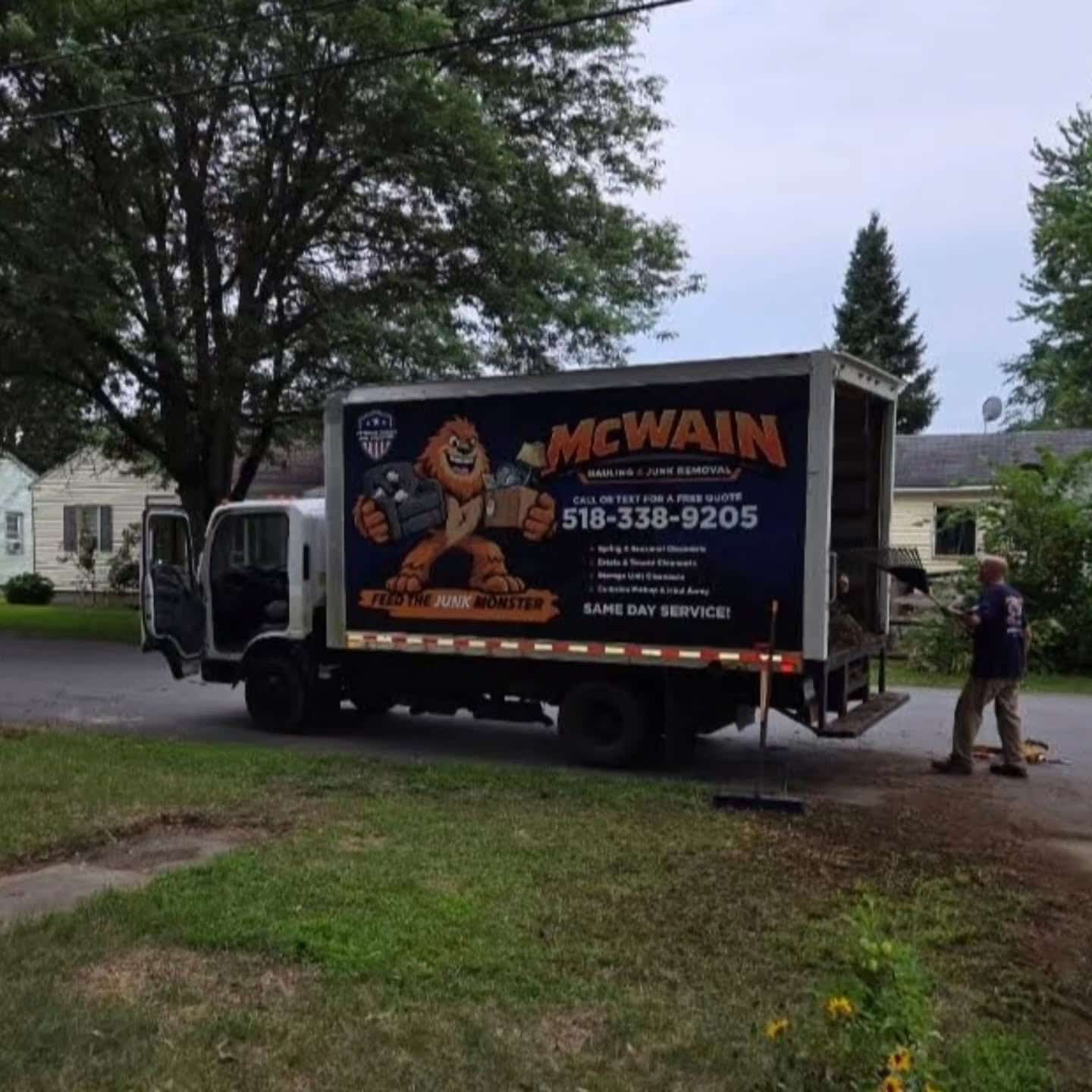 McWain box truck parked curbside on a residential street with a crew member at the back