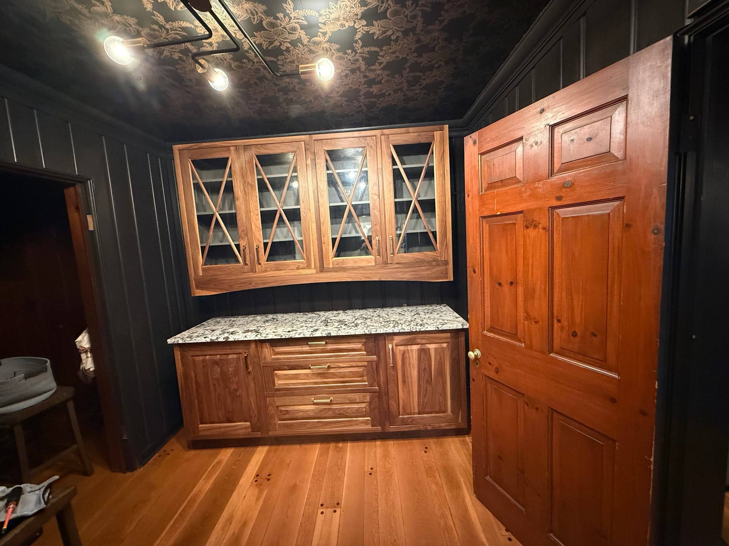 Finished wood cabinets with glass-front uppers and a granite counter installed in a dark-paneled room
